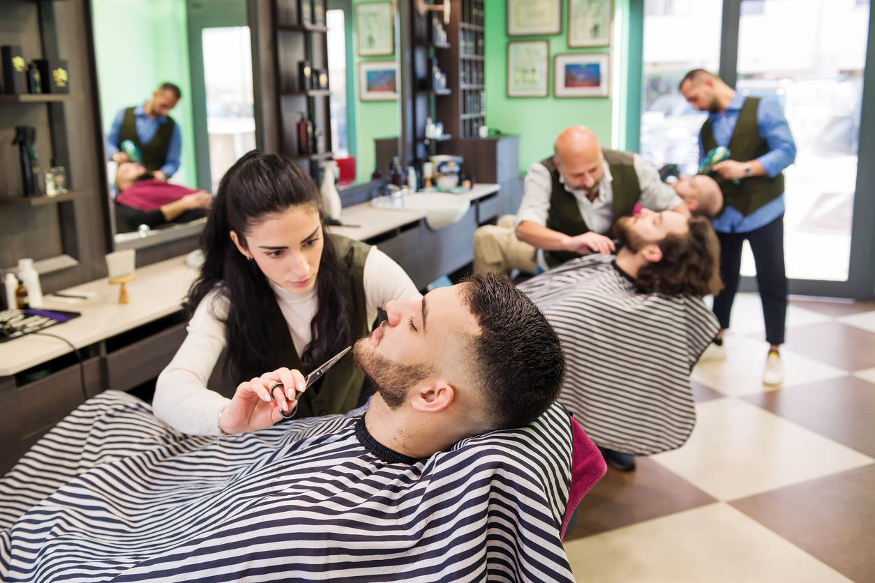 Busy barbershop with stylists attending to clients, showing the thriving business environment achieved through effective salon software management