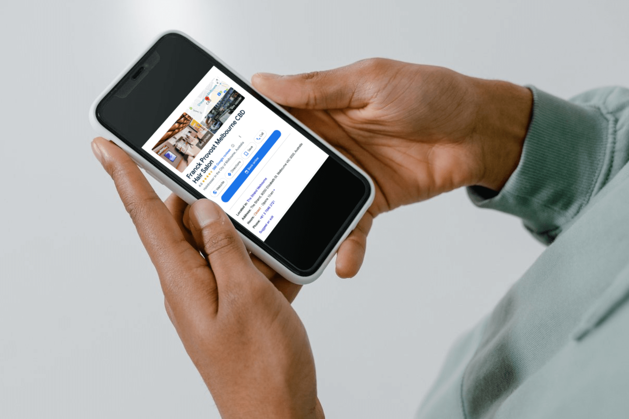 A person's hand holding a smartphone, displaying a Reserve with Google booking page for Frank Provost Melbourne CBD, a salon using Simple Salon software. The screen shows various booking options, highlighting the convenience of scheduling salon appointments directly through Google.