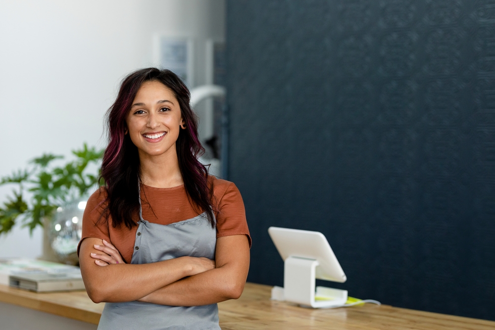 Confident & happy salon owner standing at the front desk.