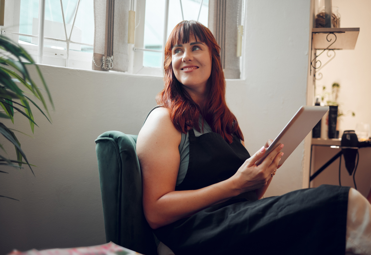 A relaxed salon professional using a tablet, representing the future of salon programs integrating advanced technology.