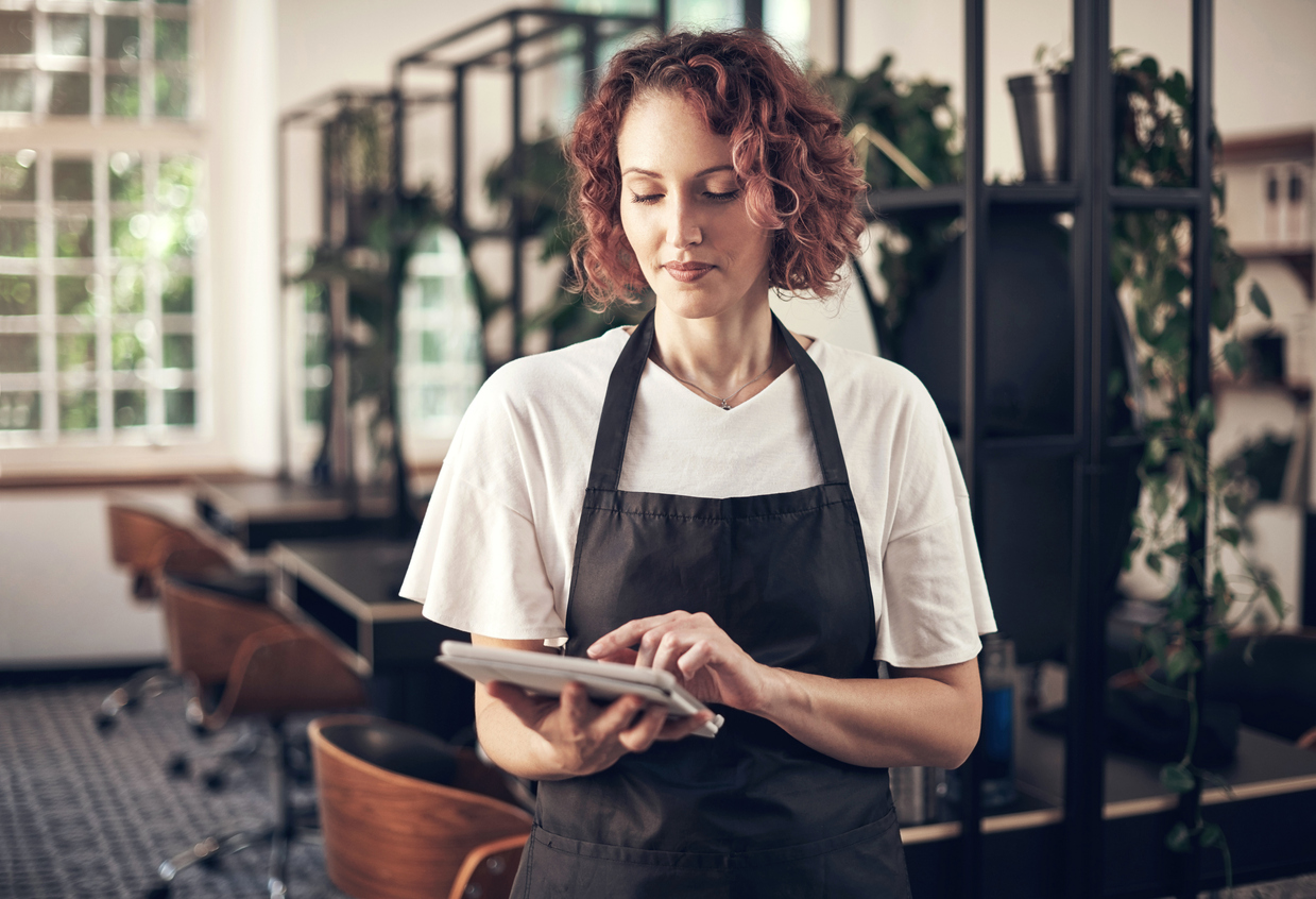 A female salon staff member using a tablet to manage appointments, illustrating the benefits of scheduling software for optimising salon operations.