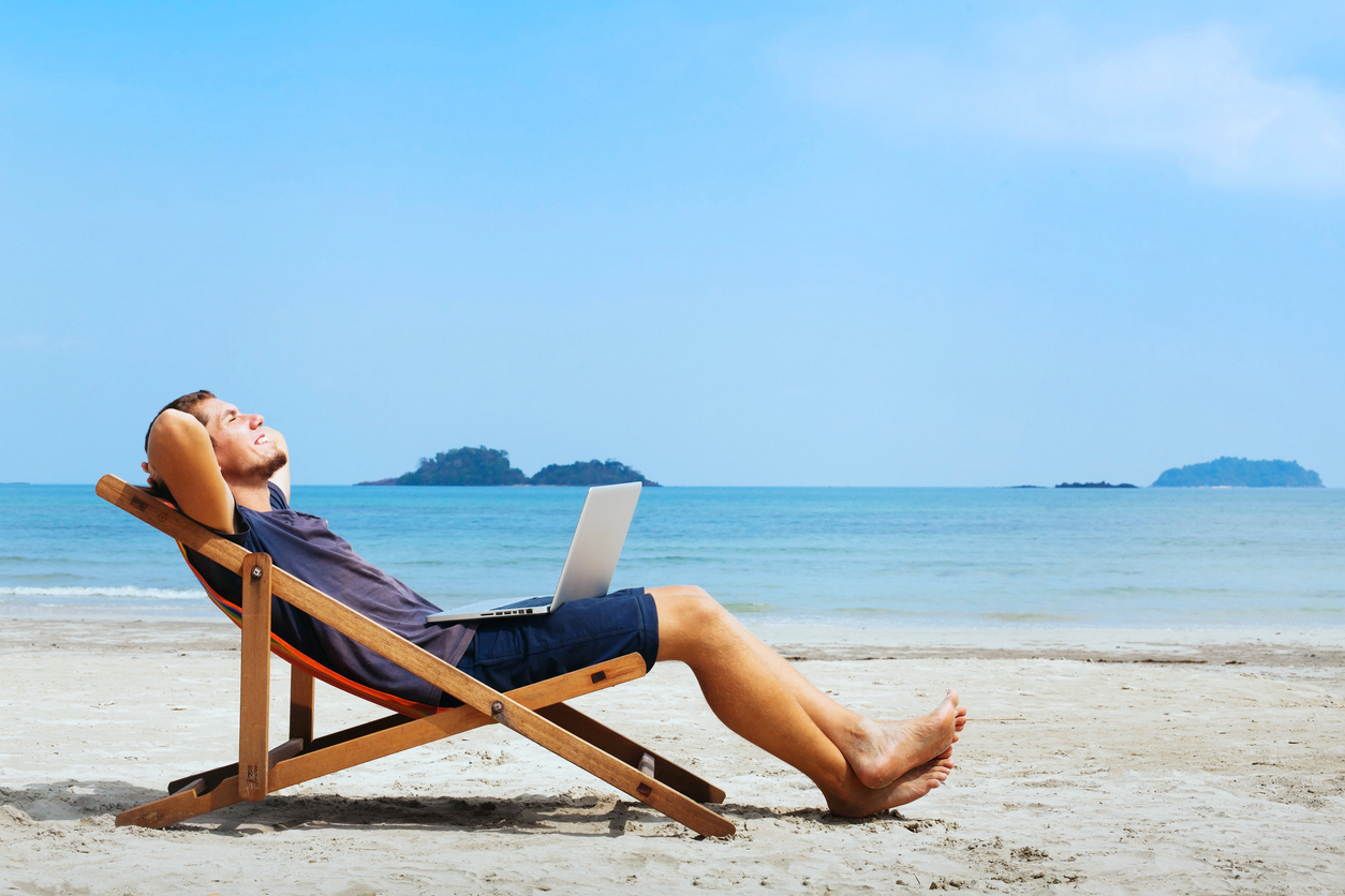 A man relaxing on a beach chair with a laptop, symbolising the ease and flexibility of using cloud-based scheduling software for salon management.