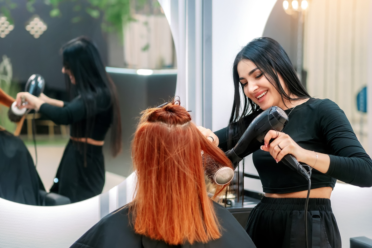 A hairstylist smiling while blow-drying a client's hair, demonstrating exceptional customer service and professional salon skills."