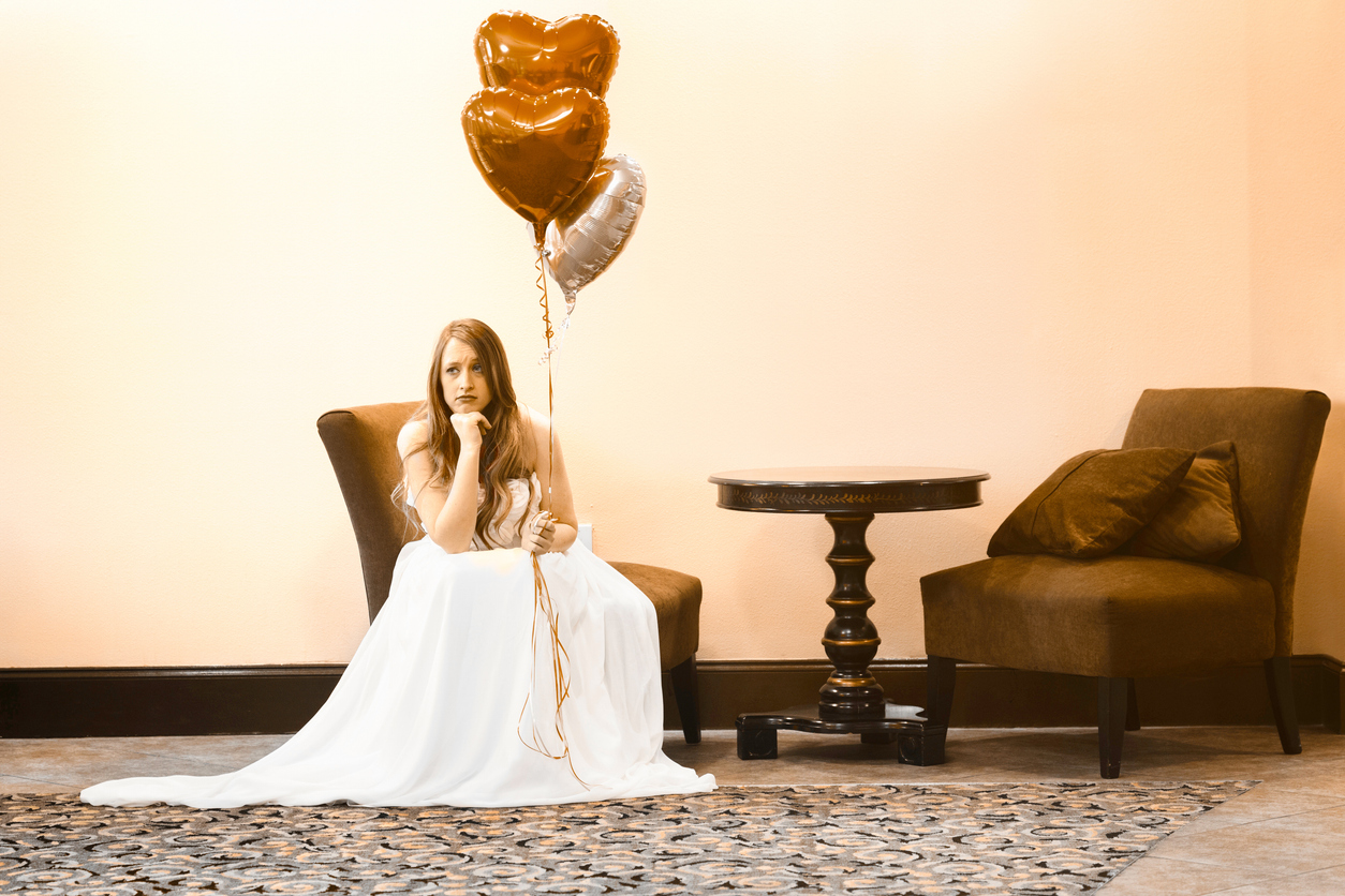 "A woman in a formal dress sits alone in a waiting area, holding heart-shaped balloons, with a disappointed expression. This image represents the frustration and impact of no-show appointments in salons."