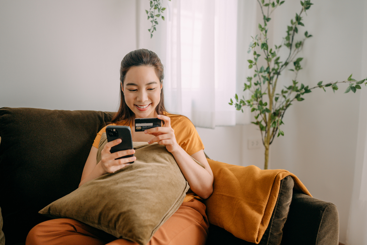 "A smiling client making an appointment online from the comfort of her home using her mobile phone and credit card, highlighting the ease and convenience of online booking for salons."