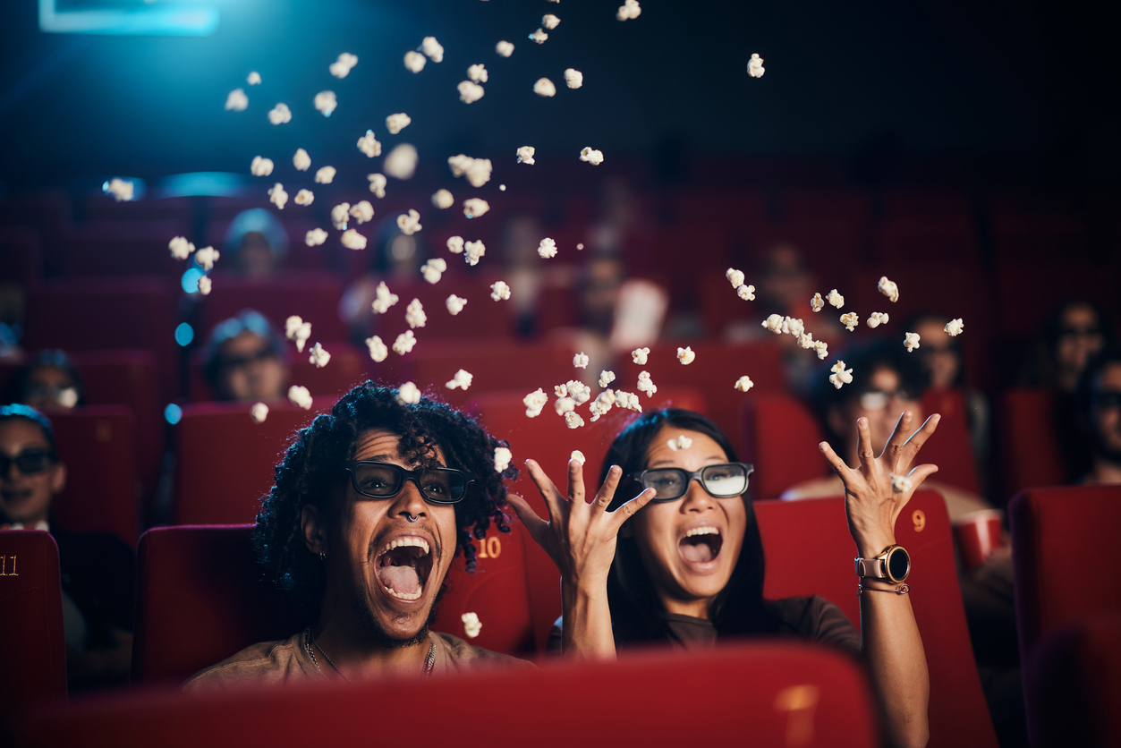 Image of two people in a movie theatre, joyfully throwing popcorn in the air, symbolising the excitement and surprise about the SMS campaign's hidden secret.