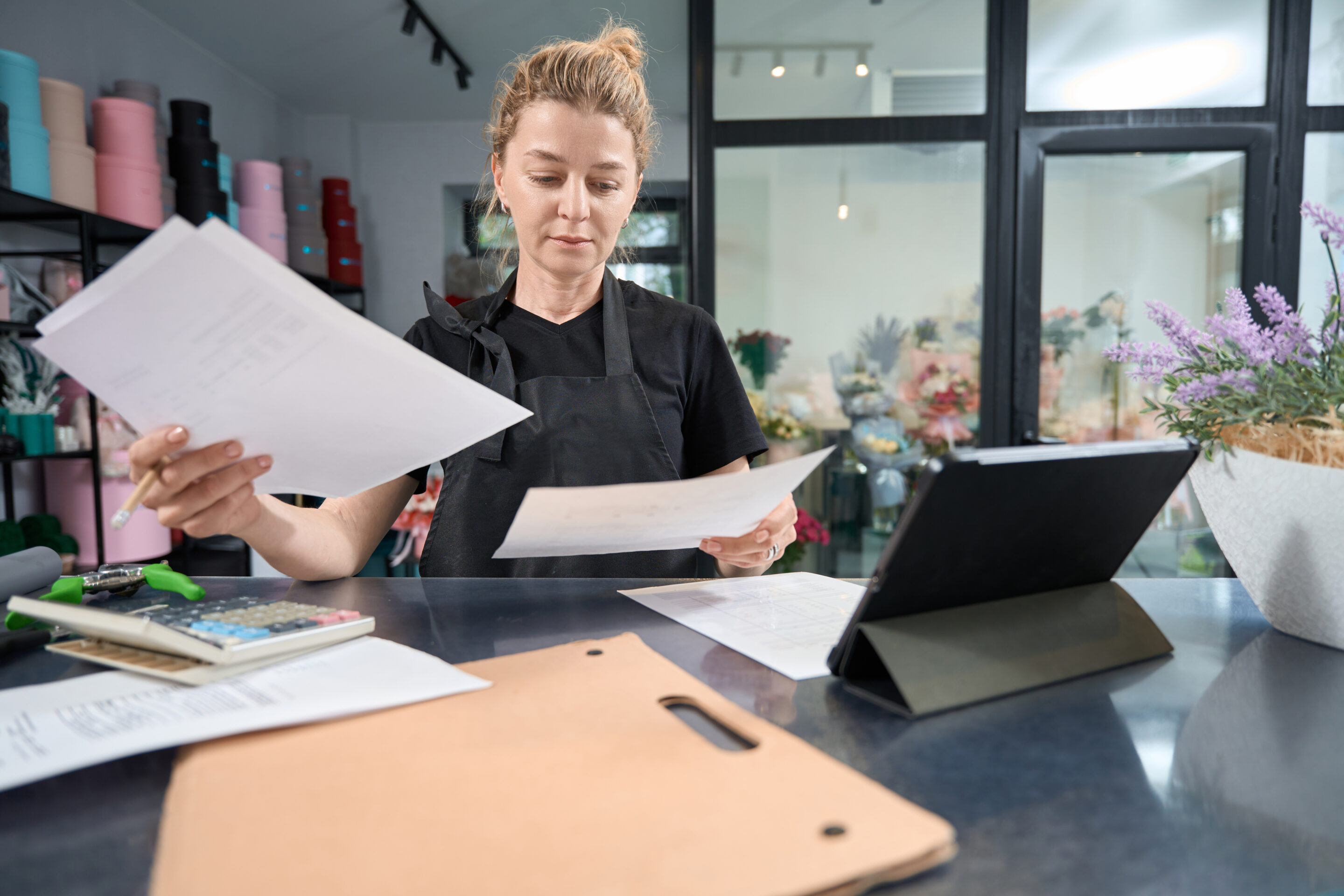 A salon owner surrounded by paperwork and seemingly overwhelmed, highlighting the time-consuming administrative tasks. Discover how salon management software can streamline these processes, freeing up valuable time to focus on clients and grow your business.